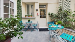 A small patio area with turquoise metal chairs and tables, a door, and potted plants. - Hotel Carladez Cambronne (Paris)