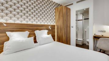 Quarto de hotel moderno com uma cama grande, cabeceira de madeira e área de chuveiro.