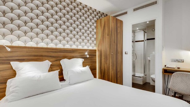 A modern hotel room with a large bed, a wooden headboard, and a shower area. - Hotel Carladez Cambronne (Paris)