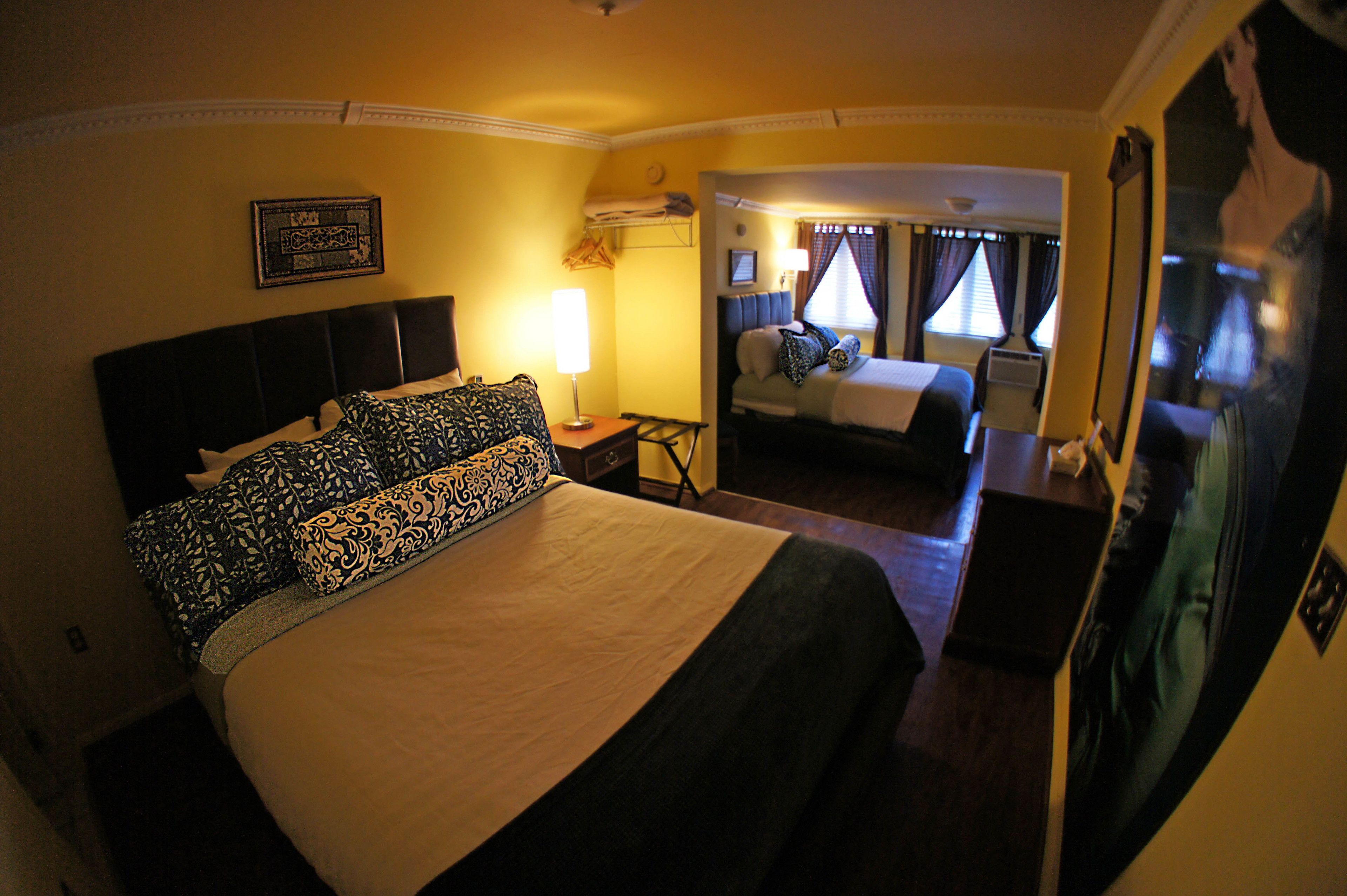 A hotel room with a large bed, a bedside table with a lamp, a small desk, and a mirror.