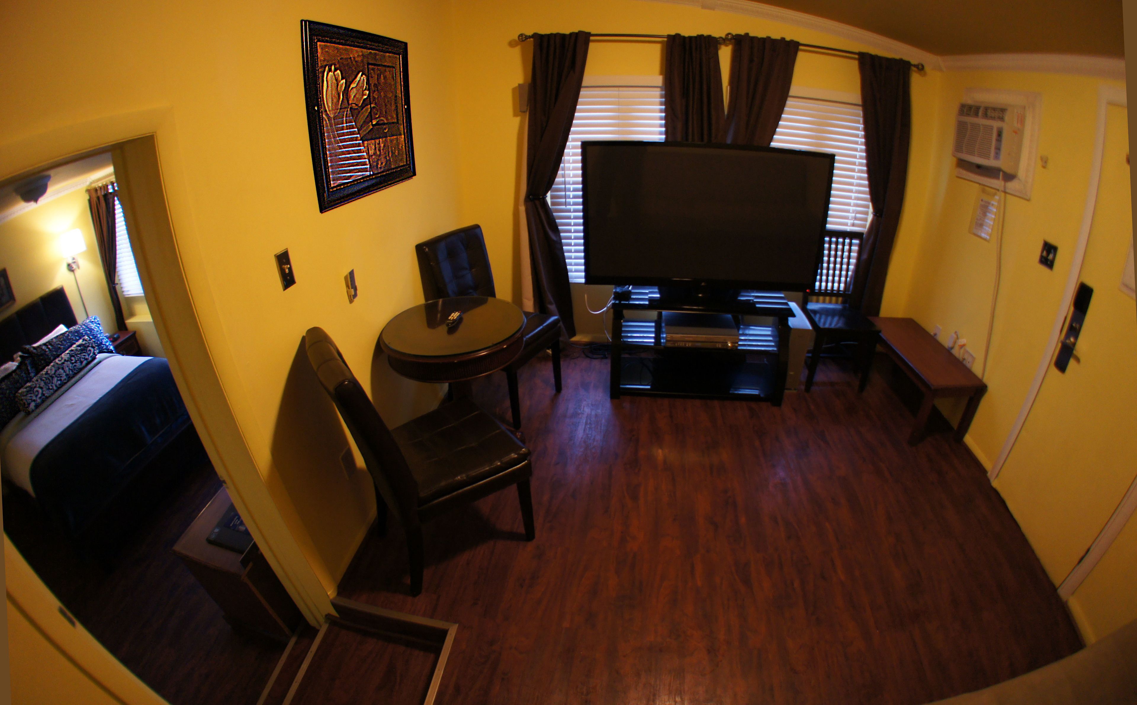 A compact hotel room with a bed, a small table, a chair, a TV, and a window with curtains.