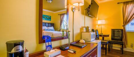 A hotel room with a bed, bedside table, coffee maker, remote controls, and a television.