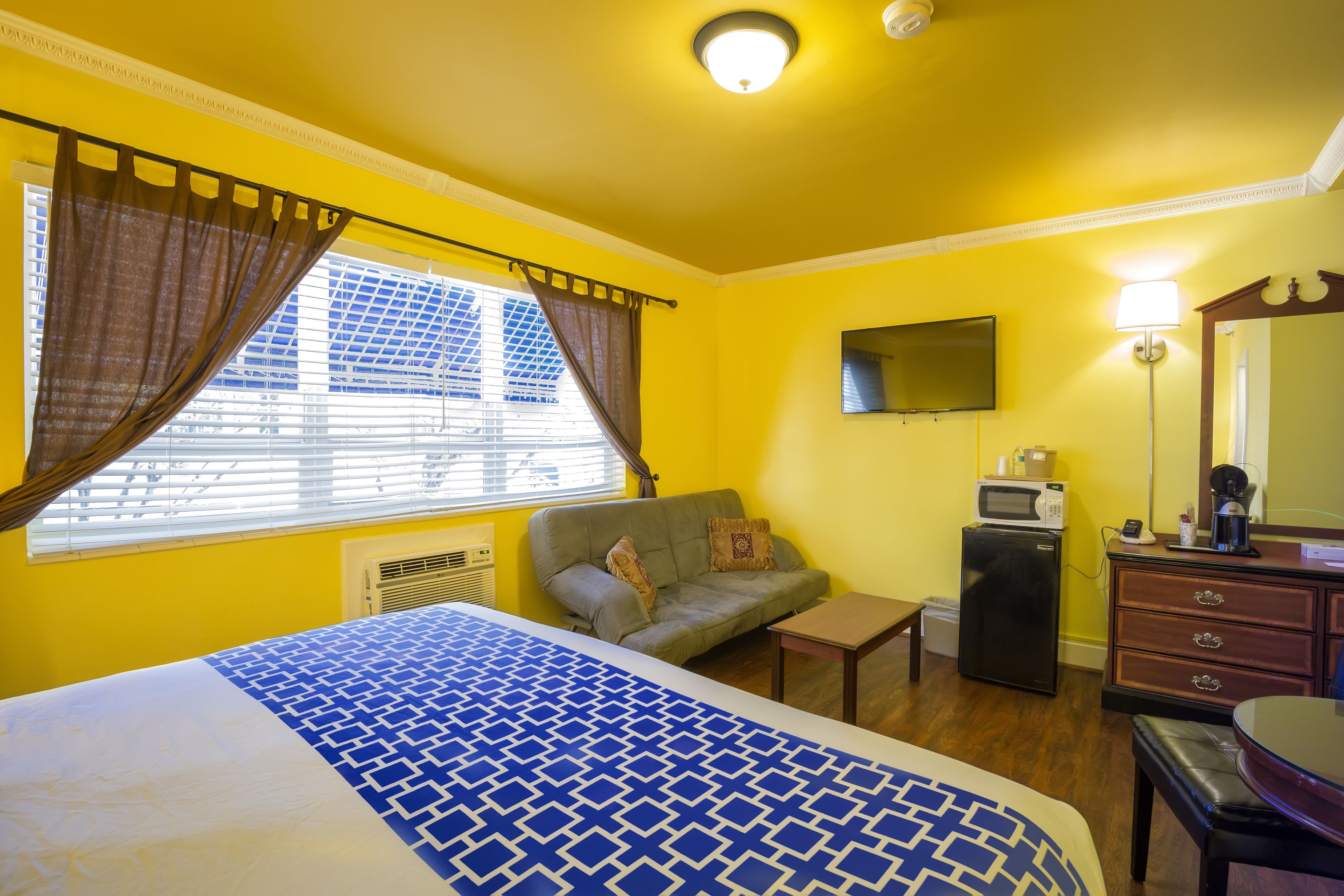 A room with a bed, a sofa, a desk, a dresser, a TV, and a microwave.