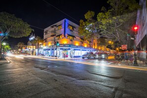 Un immeuble à plusieurs étages dont le rez-de-chaussée est aménagé en espace commercial, avec une devanture visible et un véhicule stationné.
