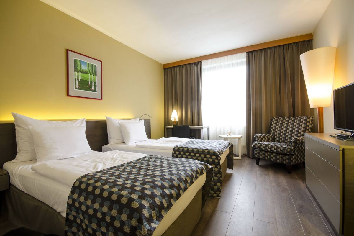 A hotel room with two beds, a desk, a chair, a TV, and a painting on the wall.