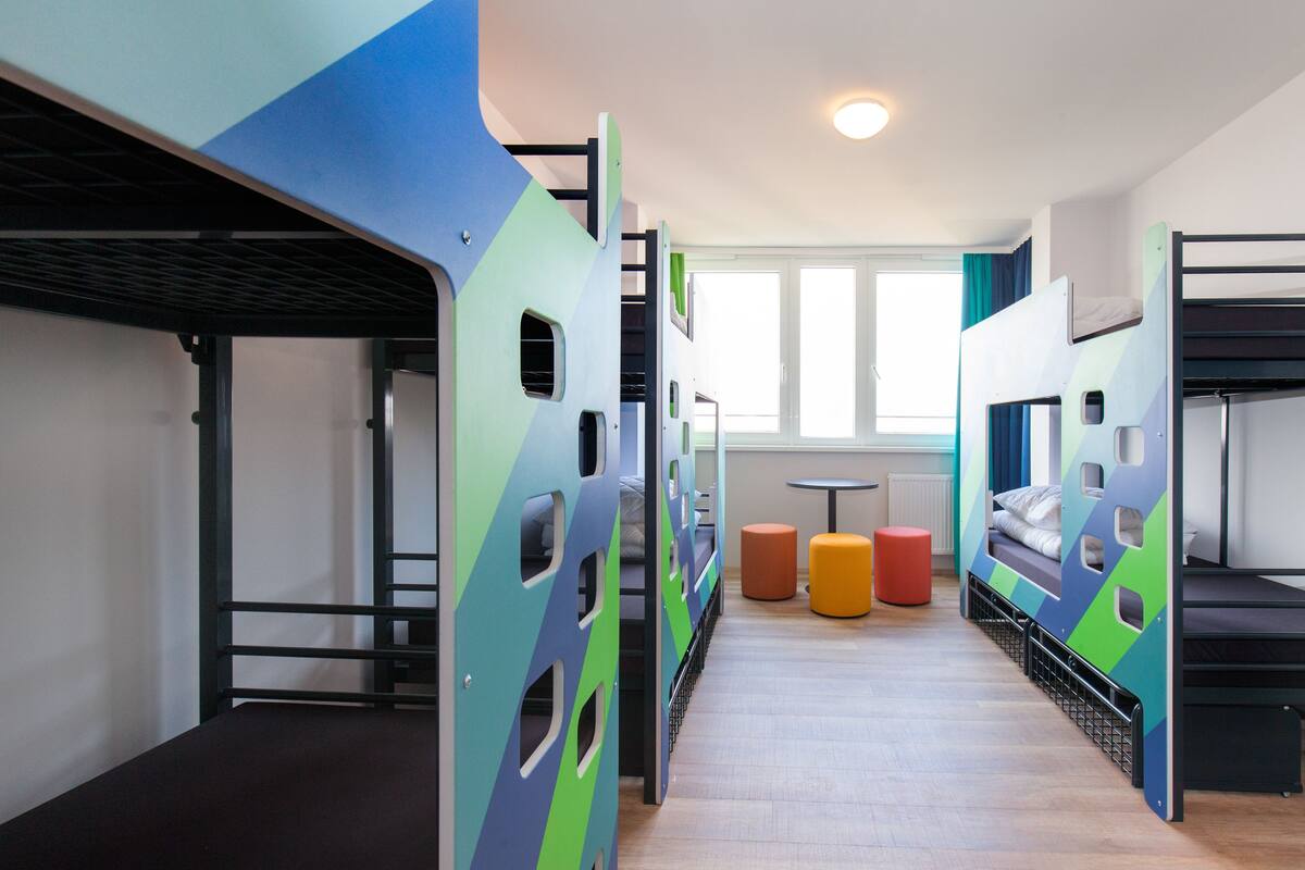 A dormitory with bunk beds, a small table, and colorful stools.
