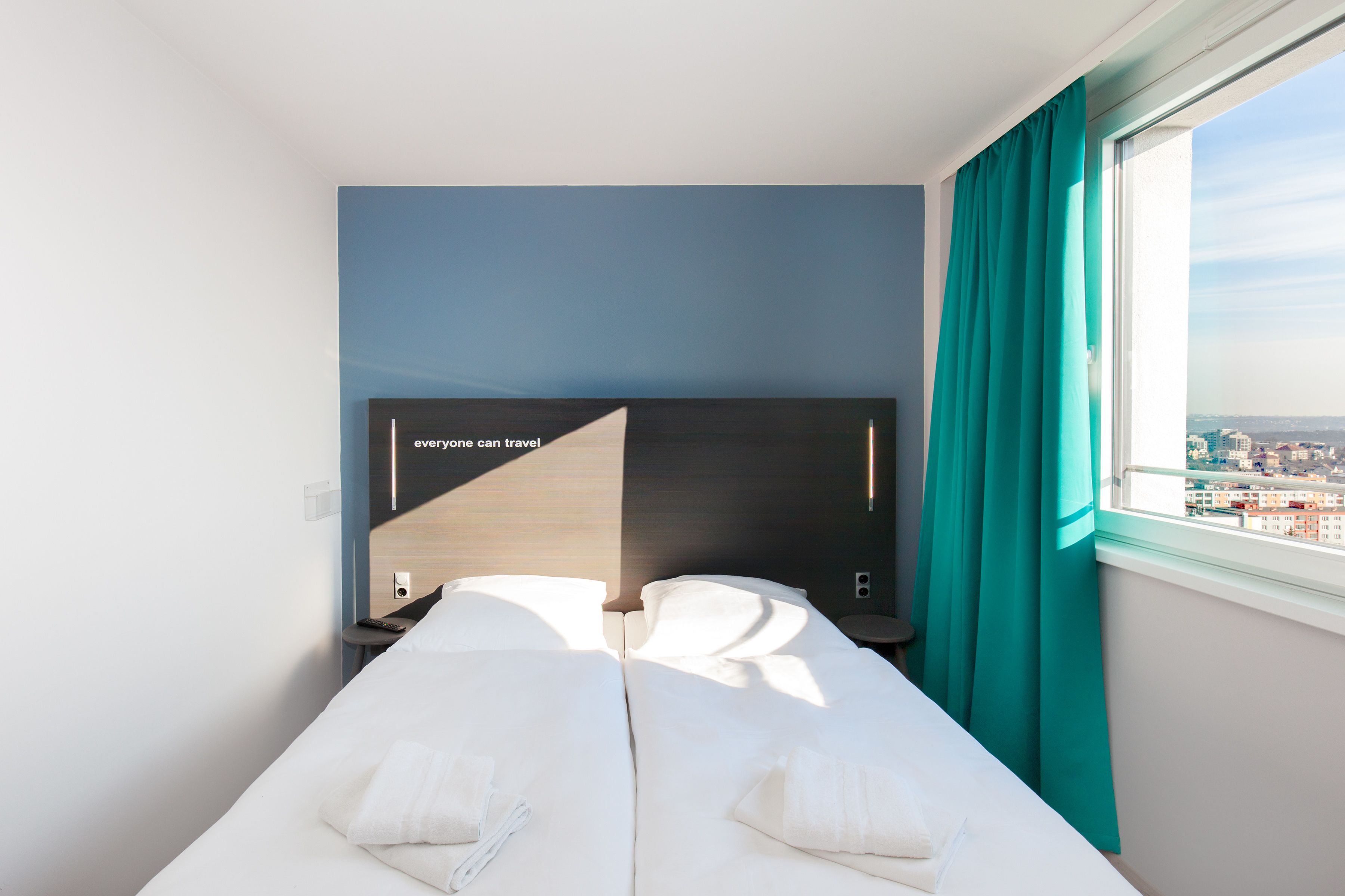 Habitación de hotel con cama, un televisor de pantalla plana grande, ventana con cortinas y vista a la ciudad.