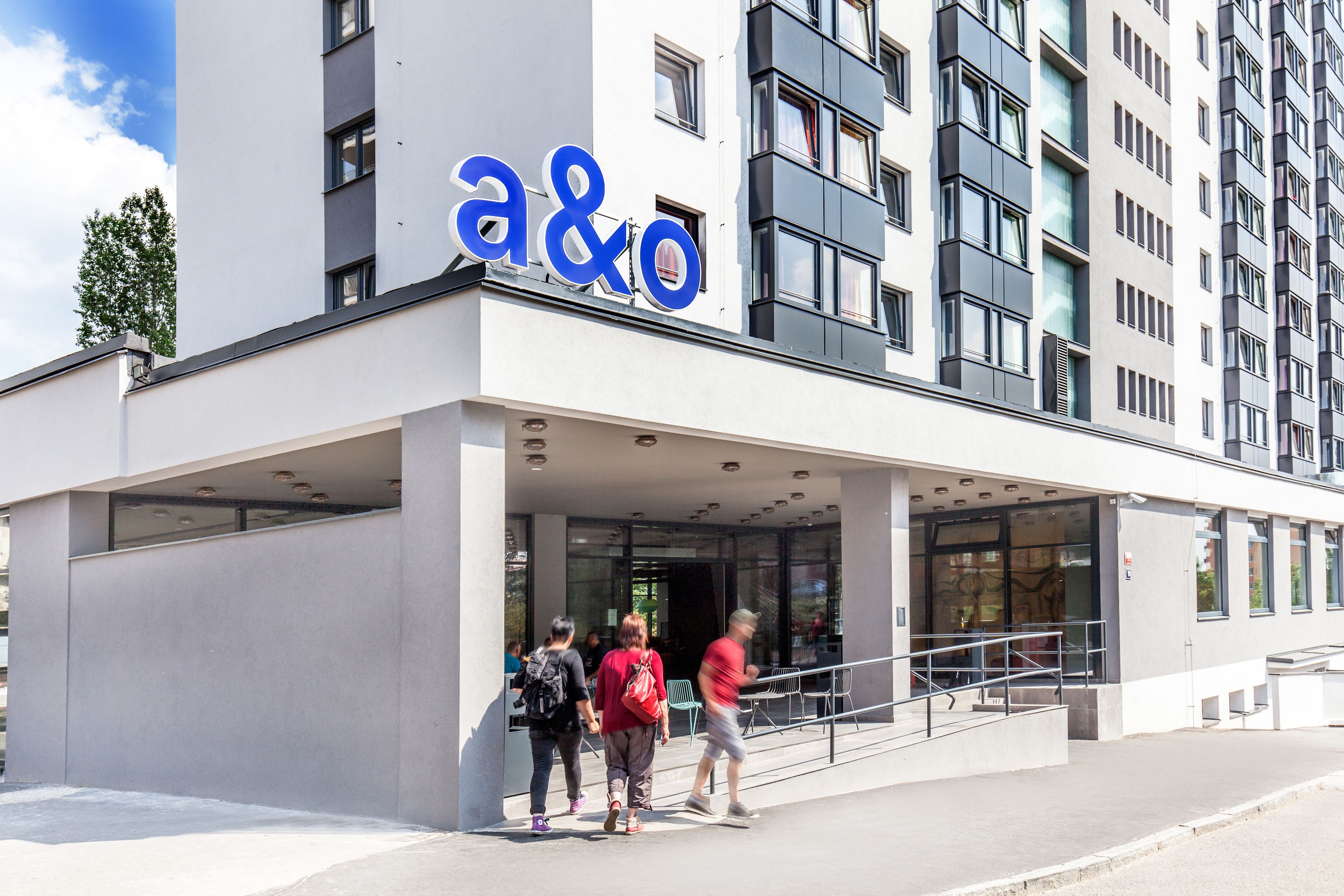 En moderne bygning med et tydeligt 'a&o'-skilt, store vinduer og et overdækket indgangsparti.
