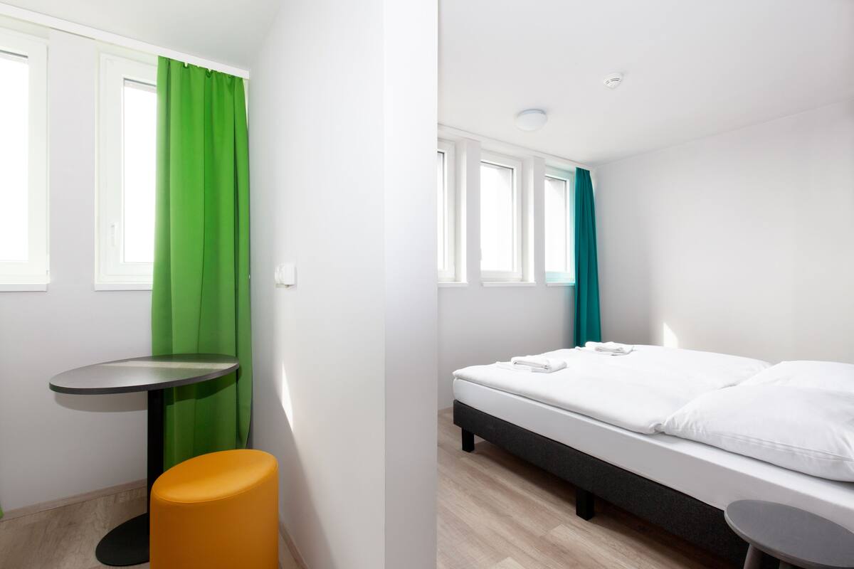 A modern room with a bed, a small table, and a stool.