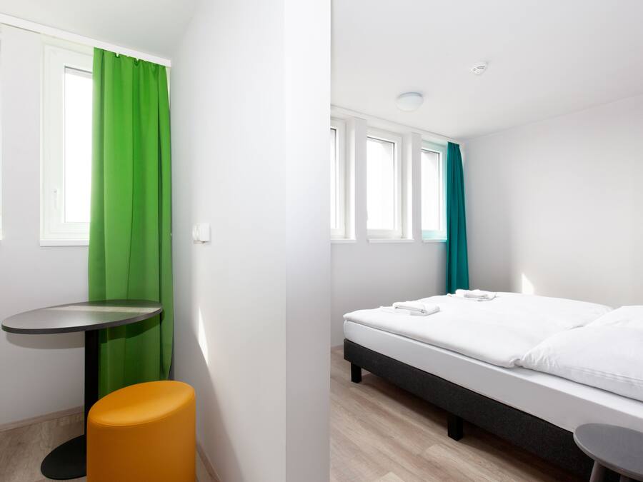 Una habitación moderna con una cama, una mesita y un taburete.