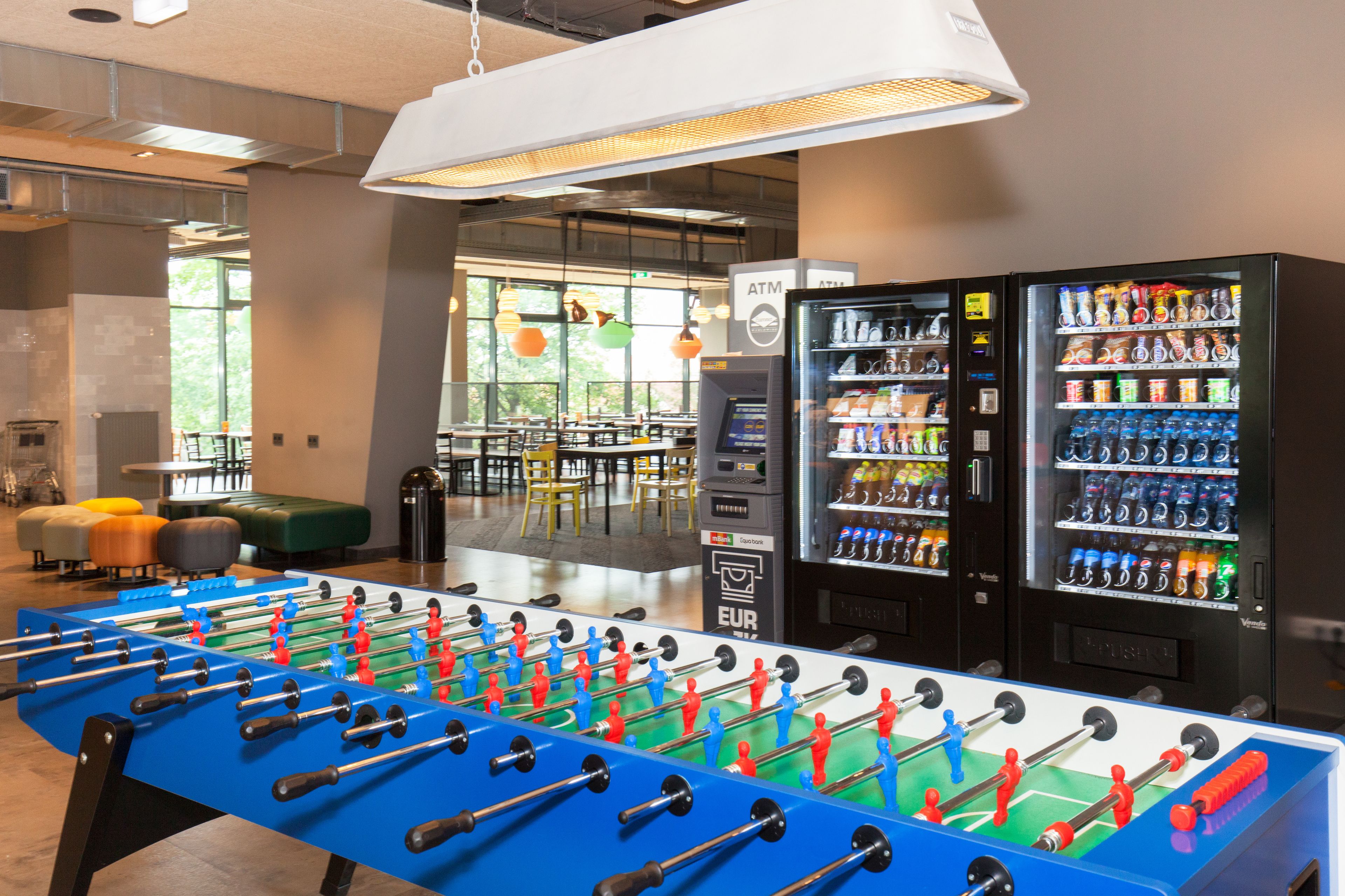 A foosball table, vending machines, and seating areas in a modern indoor space.