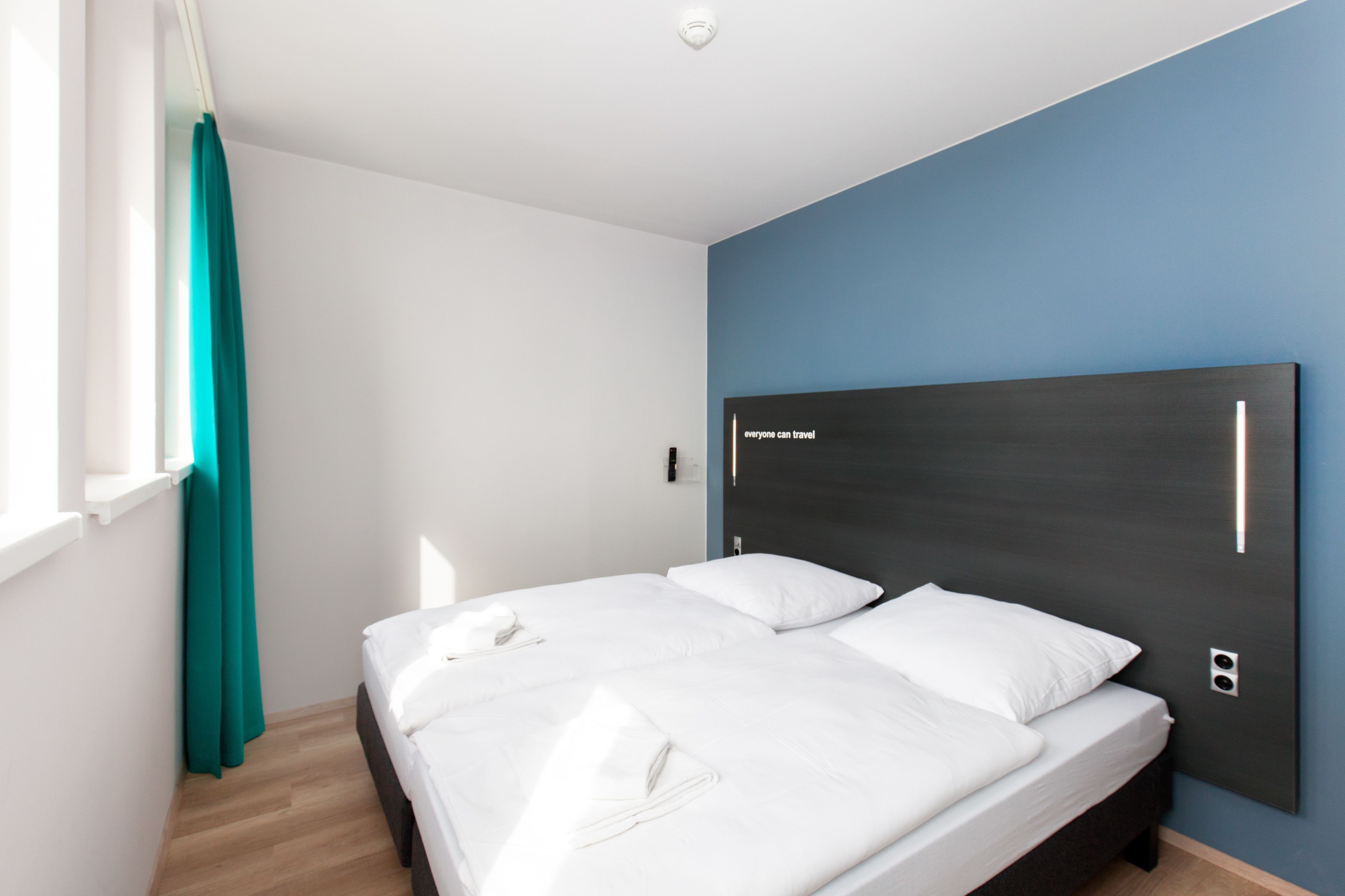 Una habitación de hotel moderna con una cama grande, cortinas color aguamarina y una pared de acento azul.