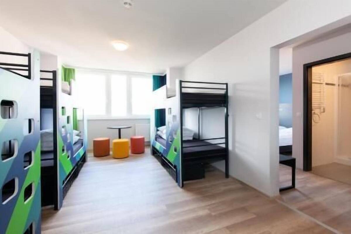 A dormitory room with bunk beds, a small table, and colorful stools.