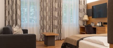 Una camera d'albergo con un letto, un divano, una scrivania, una TV e tende a motivi floreali.