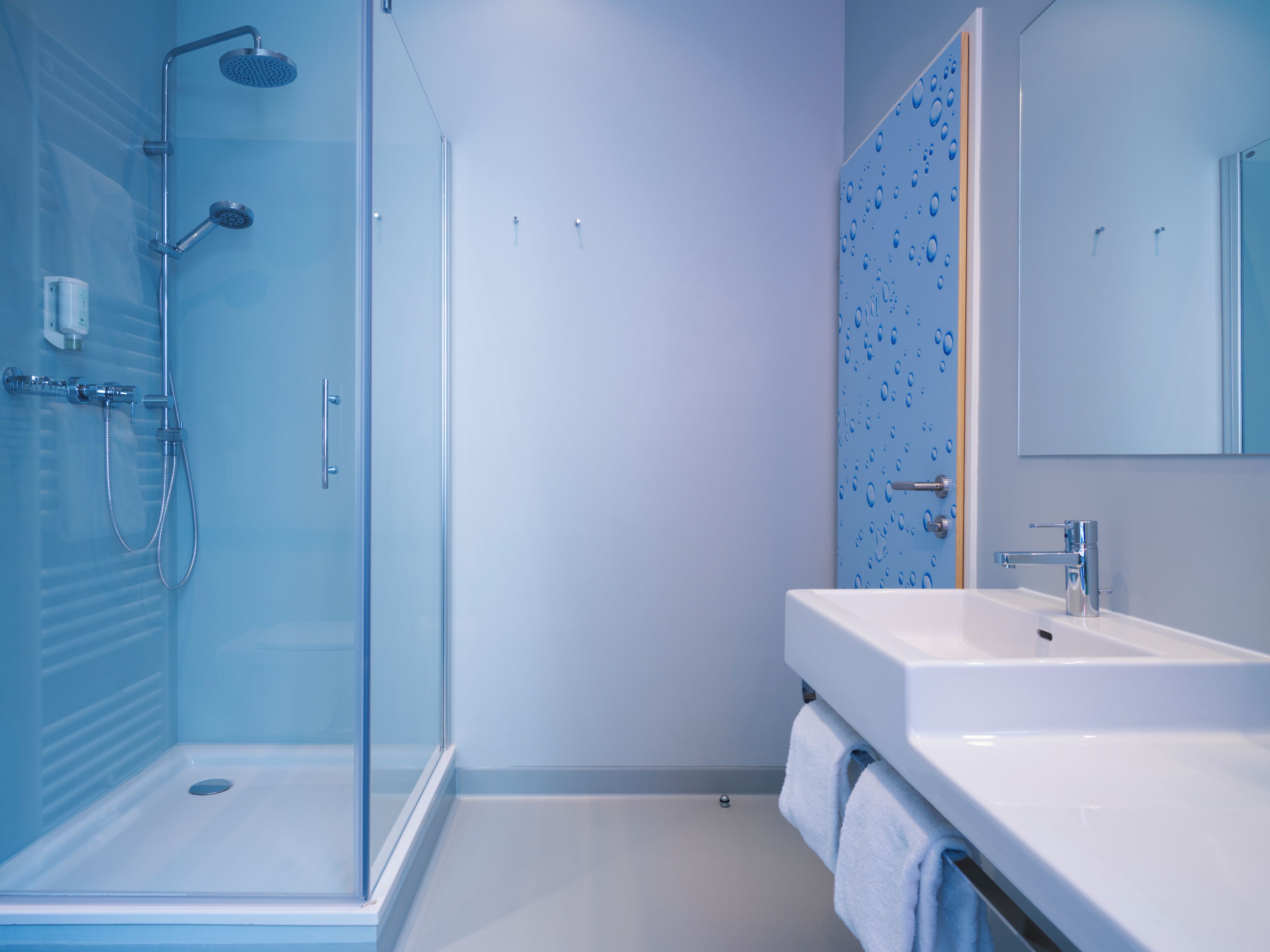 Een moderne badkamer met een douchecabine van glas, een witte wastafel en een spiegel.