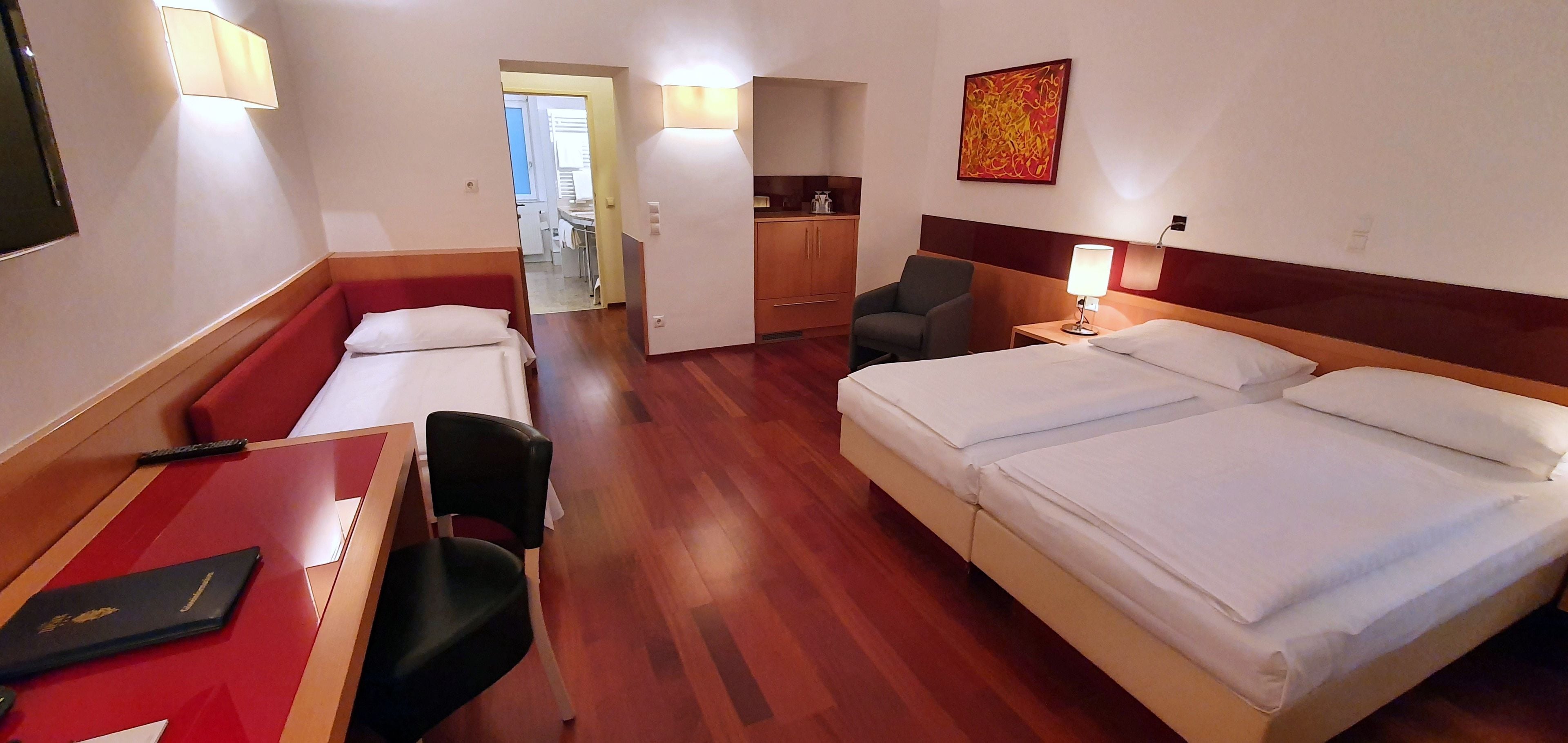 Ein Hotelzimmer mit einem Bett, einem Schreibtisch, einem Stuhl, einem kleinen Tisch, einer Lampe und einem Bild an der Wand.