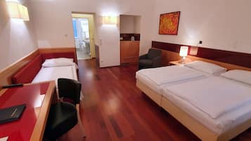 Una habitación de hotel con cama, escritorio, silla, mesita, lámpara y un cuadro en la pared.