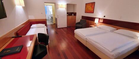 Quarto de hotel com cama, escrivaninha, cadeira, mesinha, abajur e um quadro na parede.