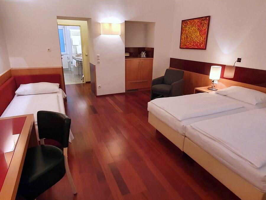 A hotel room with a bed, a desk, a chair, a small table, a lamp, and a painting on the wall.