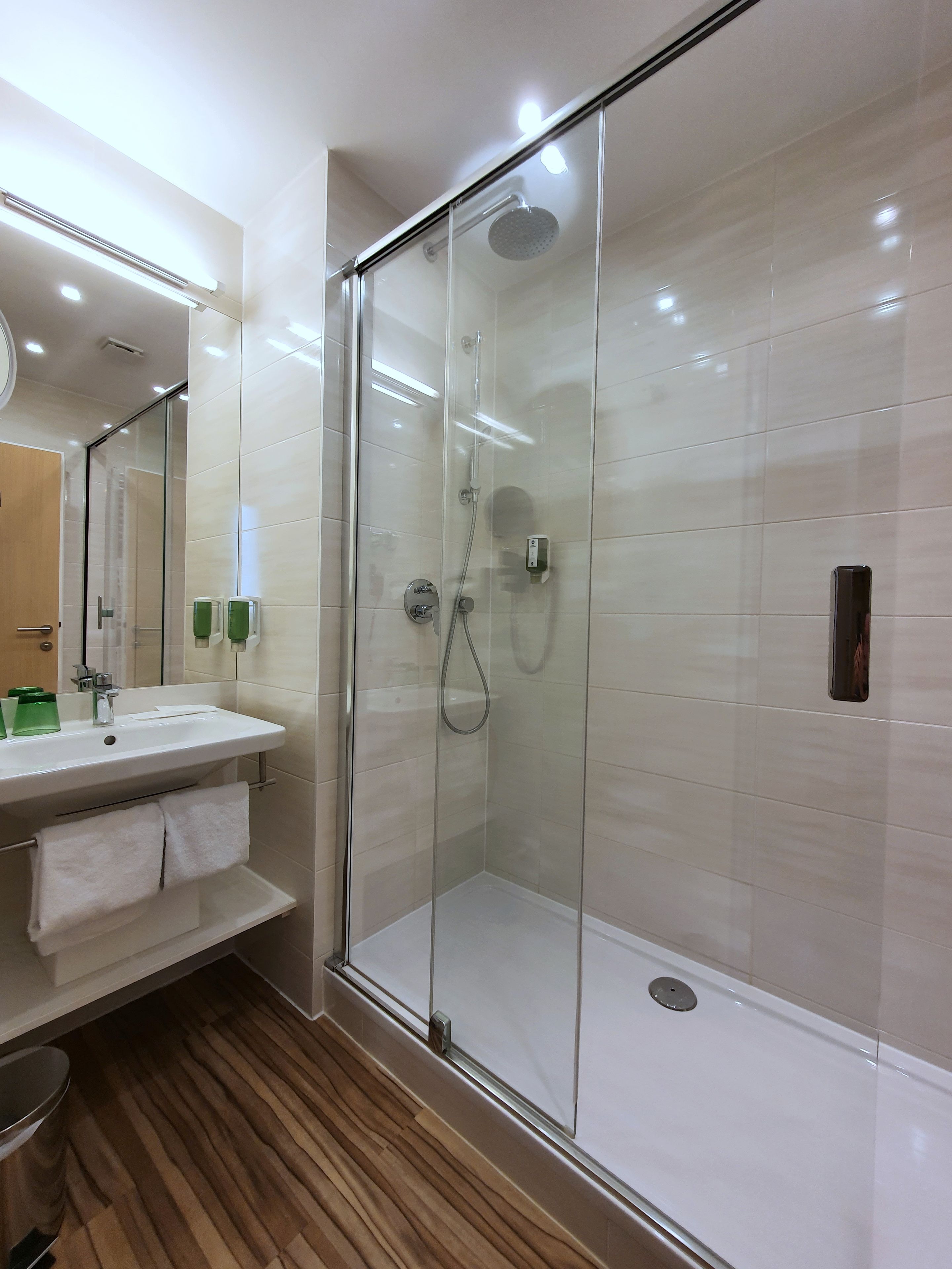 Een moderne badkamer met een douchecabine van glas, een wit wastafeltje en een spiegel erboven.