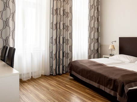 A hotel room with a bed, bedside table, lamp, and a chair.