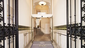 L’entrée d’un hôtel, avec un escalier en marbre, des rampes en fer forgé noir et un tapis bleu orné du nom de l’hôtel.