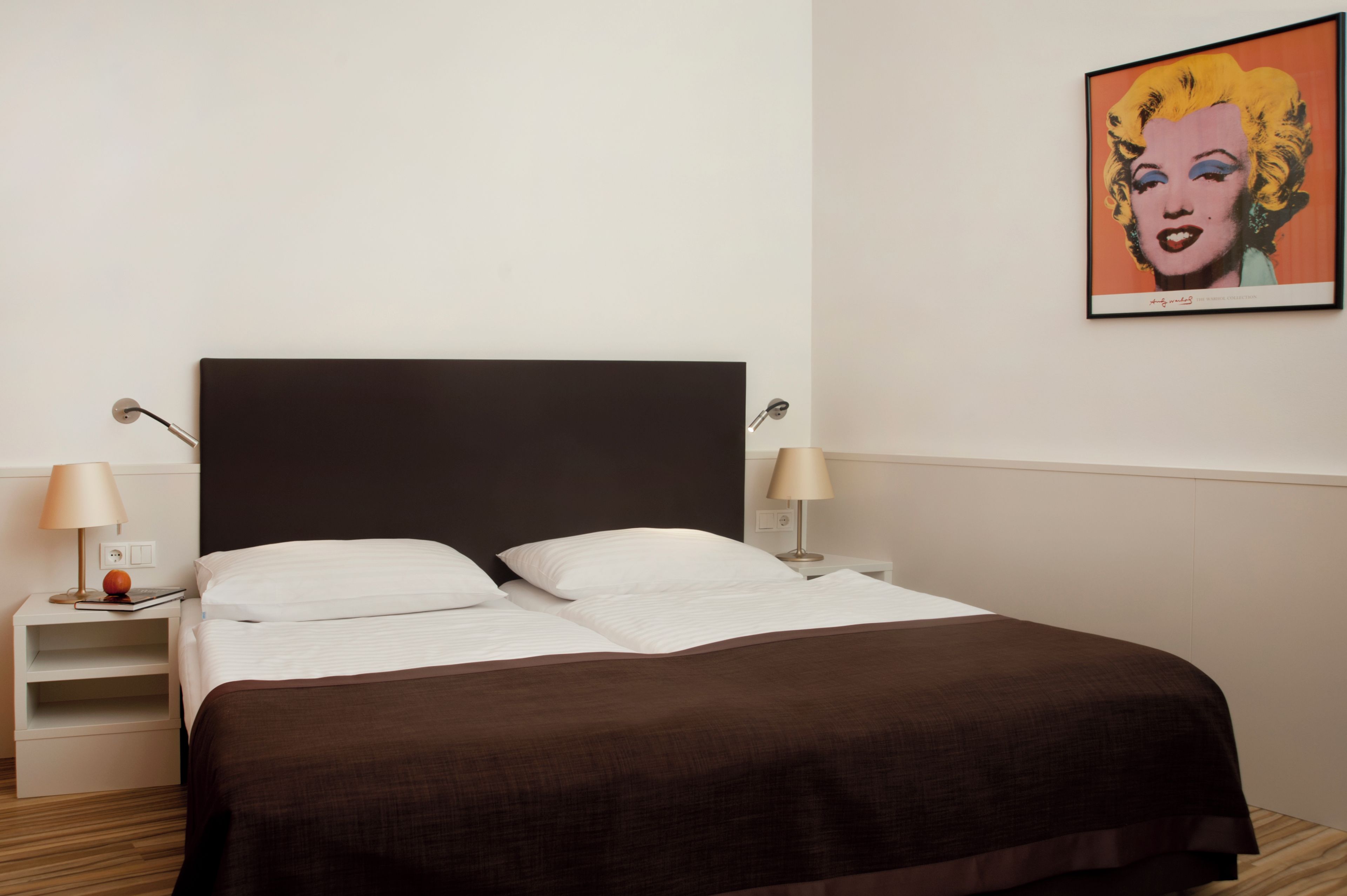 A hotel room with a bed, two bedside lamps, a nightstand, and a framed picture on the wall.