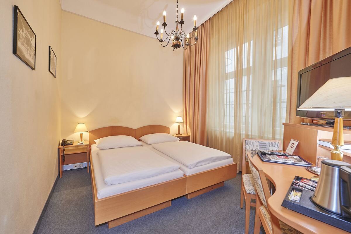 A hotel room with a double bed, bedside lamps, a desk with a lamp, a television, and a window with curtains.
