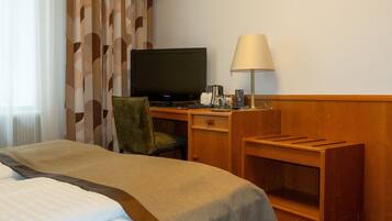 Ein Hotelzimmer mit einem Bett, einem Schreibtisch mit Fernseher, einem Sessel, einer Lampe und einem kleinen Regal.