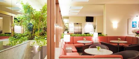 A hotel lobby with a seating area, a reception desk, and a television on the wall.