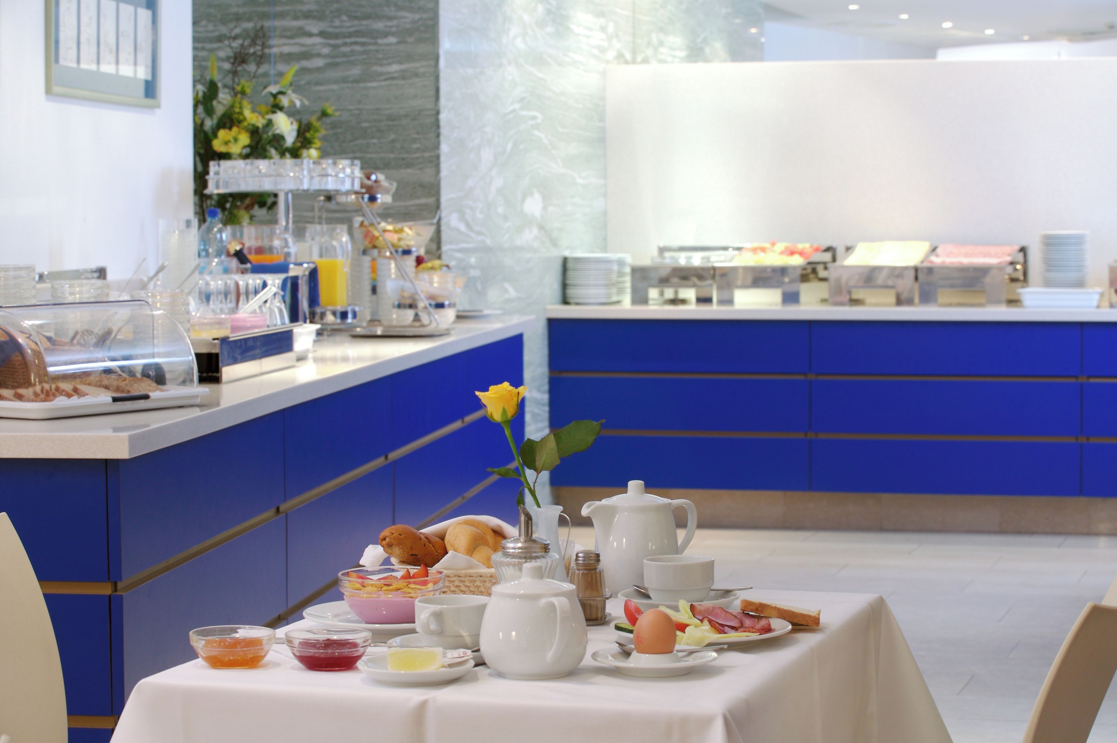 A breakfast buffet with various food items and a vase with a yellow flower on a table.