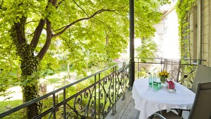 Un espace extérieur aménagé, abrité et doté d’une table pour deux, entouré d’une végétation luxuriante et offrant une vue sur un bâtiment.