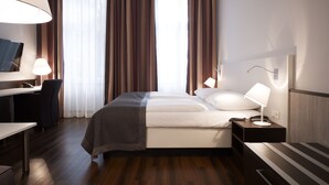 Une chambre d’hôtel moderne équipée d’un lit, de tables de chevet, d’un bureau et d’une télévision.