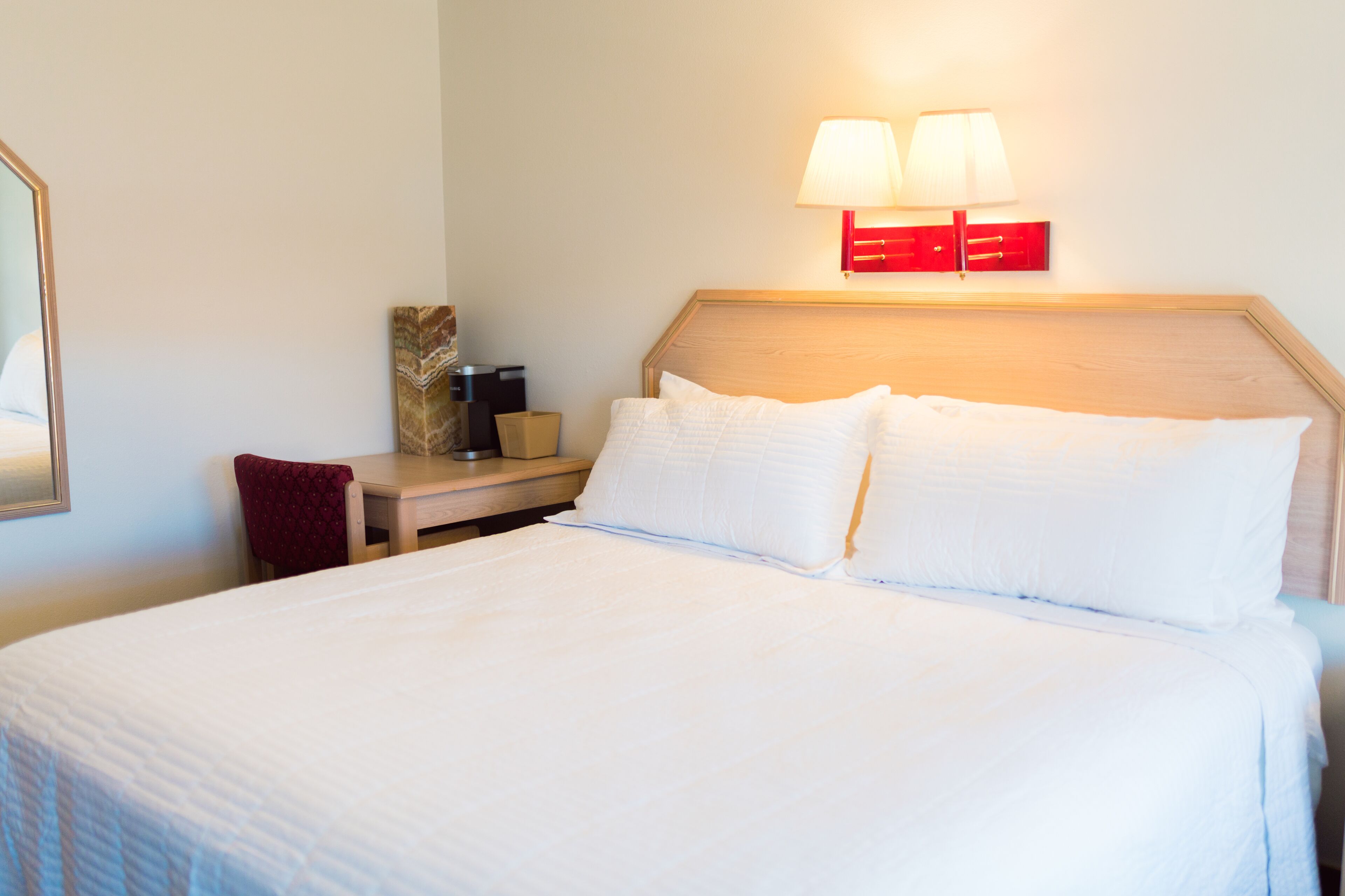 Habitación de hotel con una cama bien hecha, una mesita de noche con lámpara y un pequeño escritorio con silla.