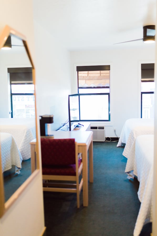 Habitación de hotel con dos camas individuales, un escritorio con una computadora, una silla y una ventana con persianas.