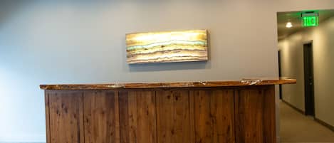 A wooden reception desk with a textured wall art piece above it and an exit sign in the background.