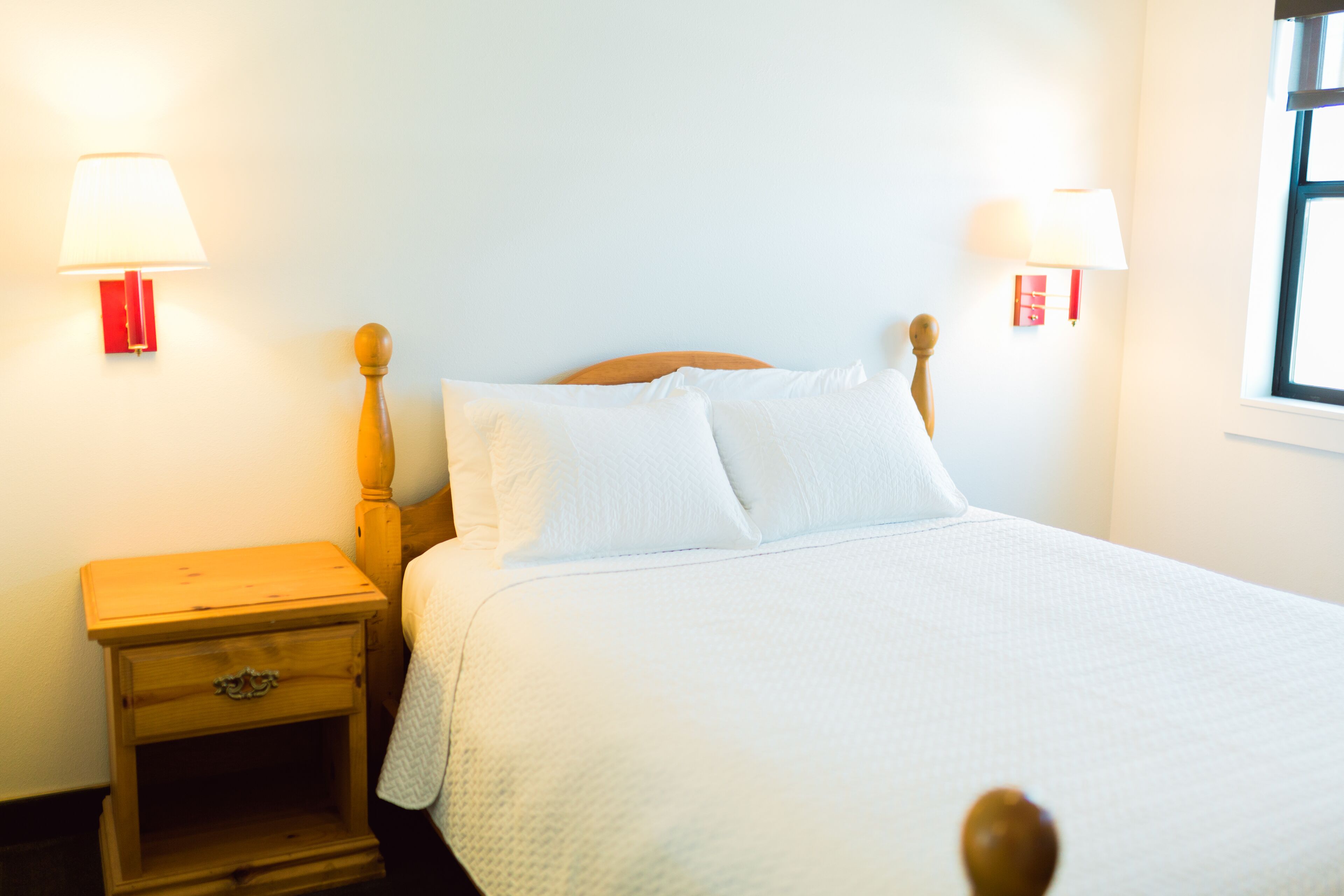 A neatly made bed with white bedding, a wooden headboard, and two bedside lamps with red bases.