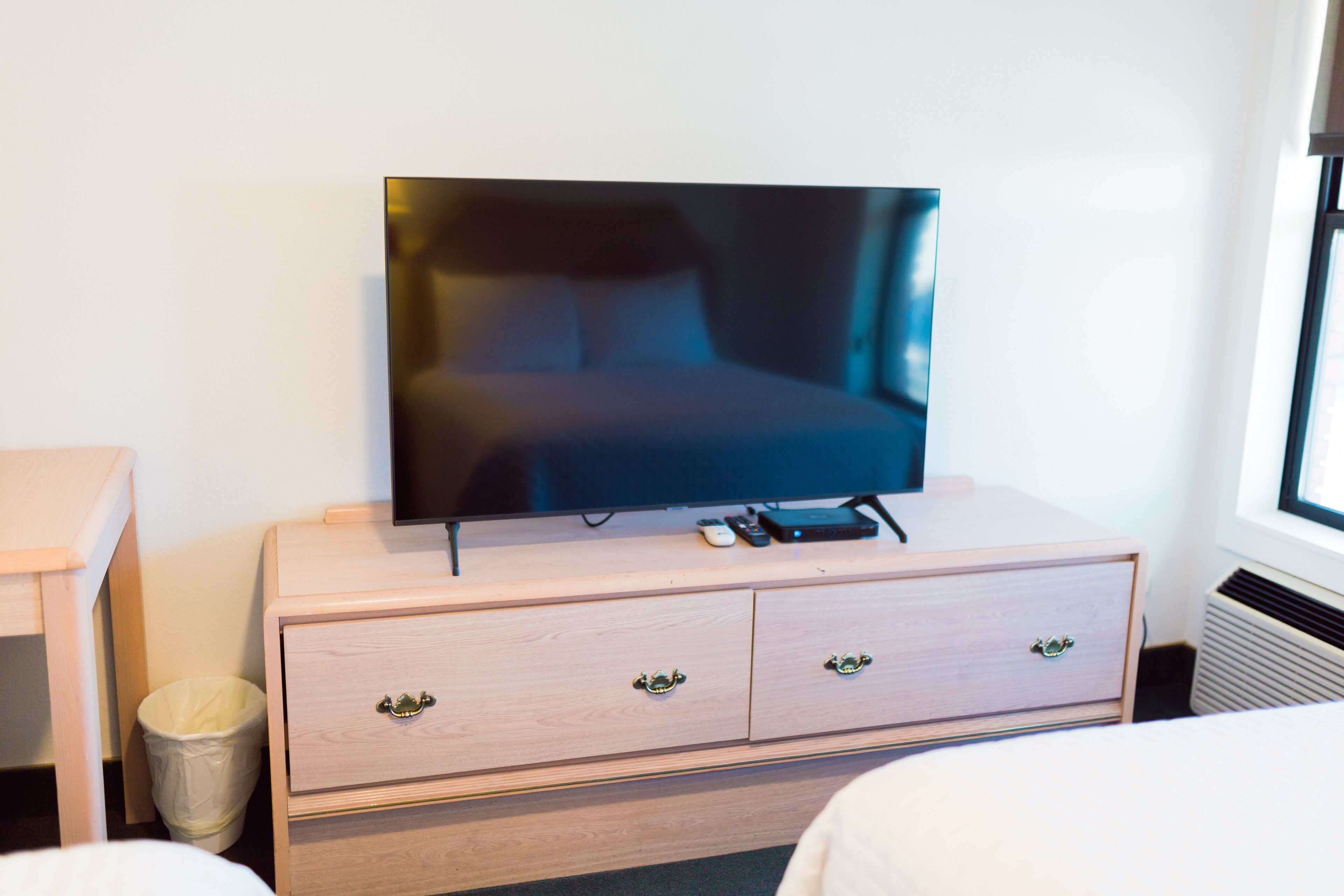 Habitació d'hotel amb un televisor sobre una petita taula de fusta, un llit i una finestra.