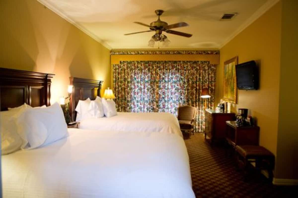 A hotel room with a large bed, a ceiling fan, a desk with a chair, and a television on the wall.