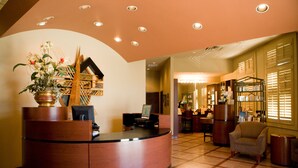 A reception area with a curved desk, a potted plant, and a seating area with a chair and a small table.