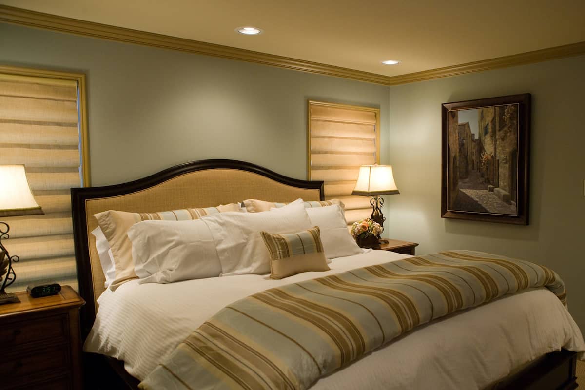 A neatly made bed with a striped blanket, two bedside lamps, and a painting on the wall.