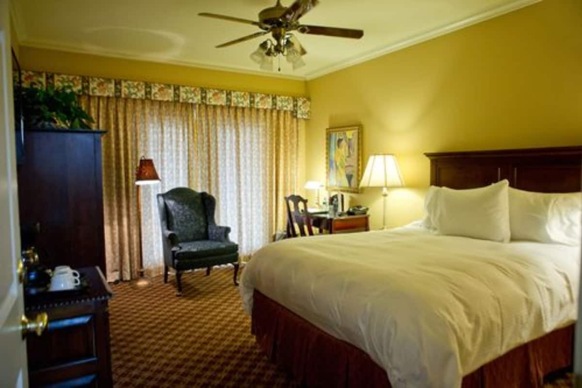A hotel room with a large bed, a desk with a lamp, a chair, and a ceiling fan.