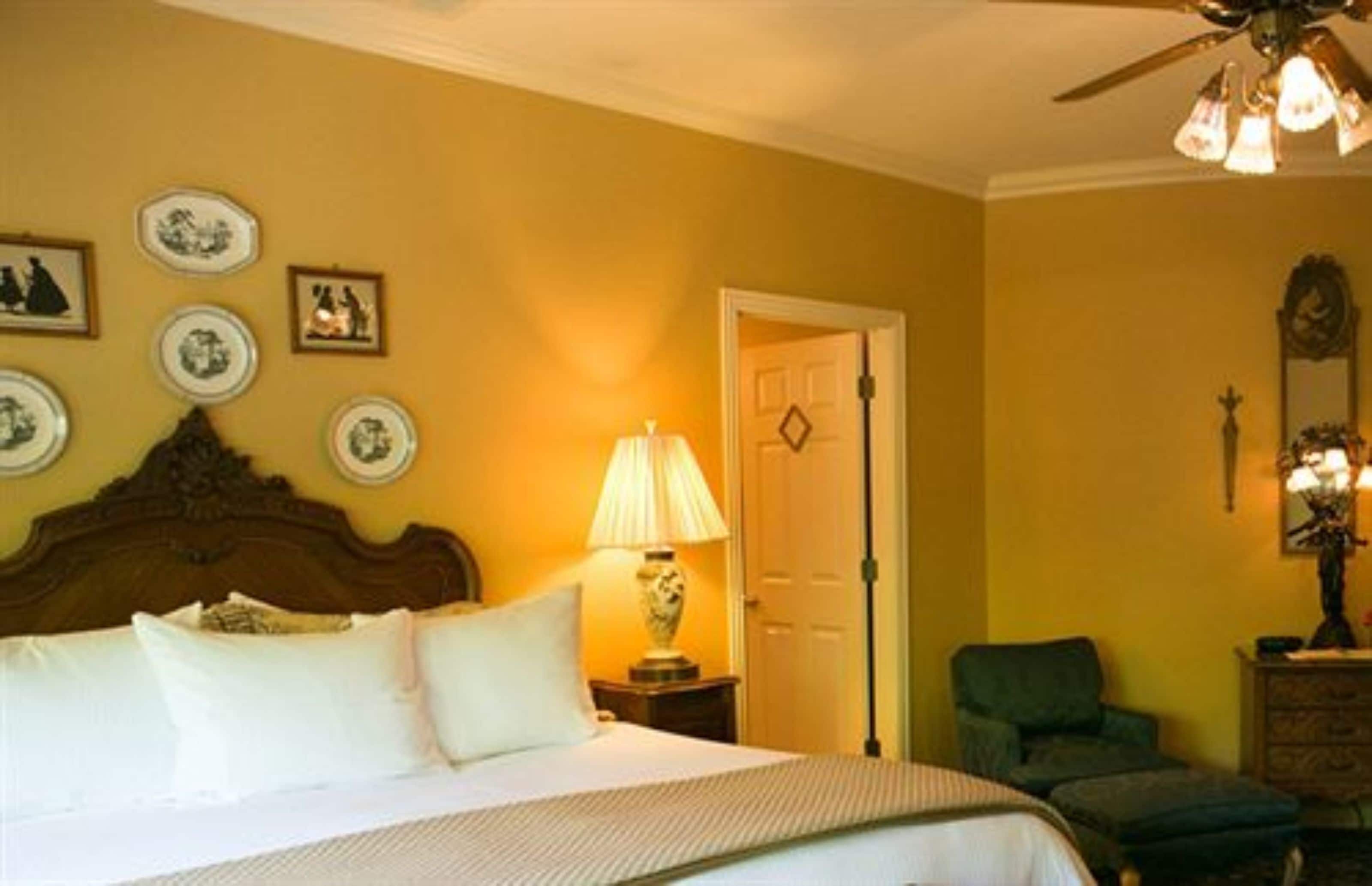 A hotel room with a bed, a chair, a lamp, and wall decorations.