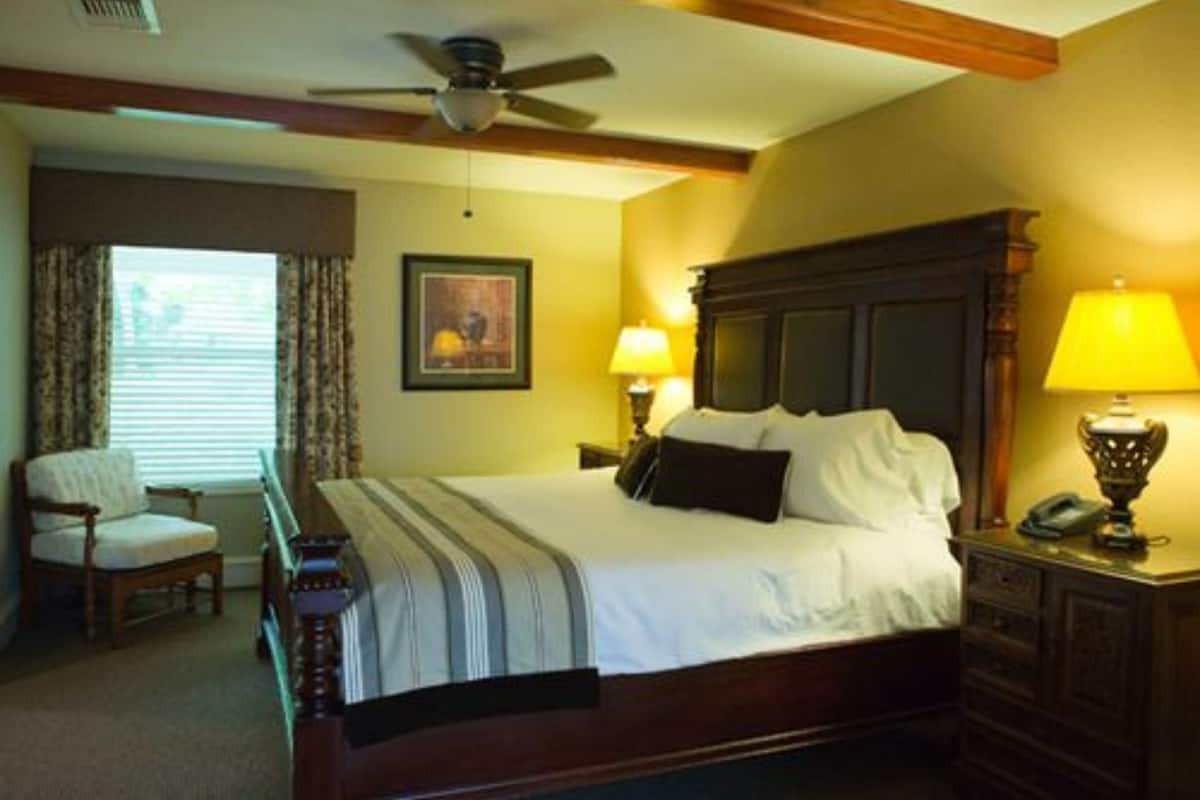 A neatly arranged bedroom with a bed, bedside lamps, a chair, and a ceiling fan.
