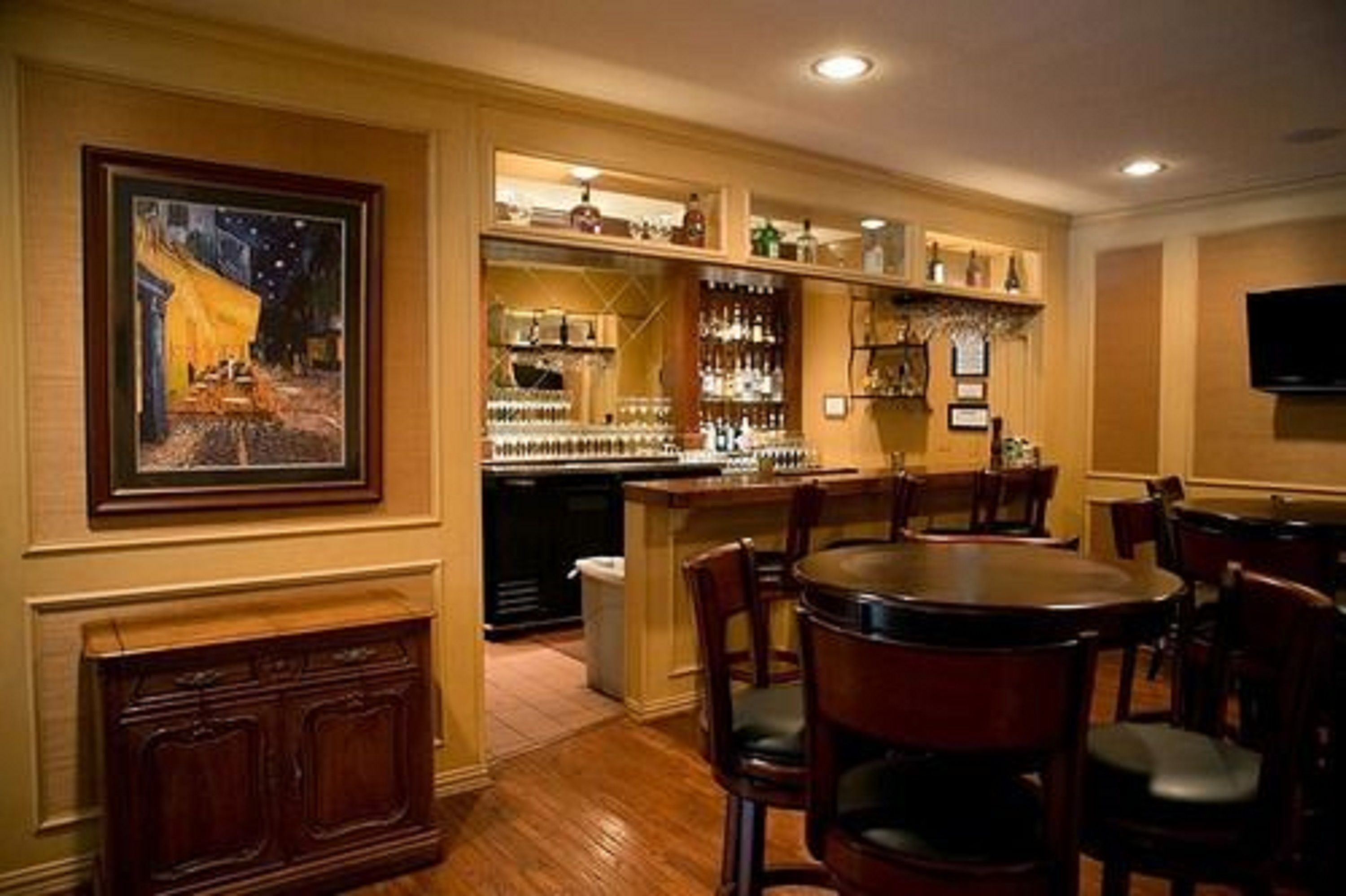 Zona de bar con muebles de madera, un cuadro en la pared y estantes con botellas.
