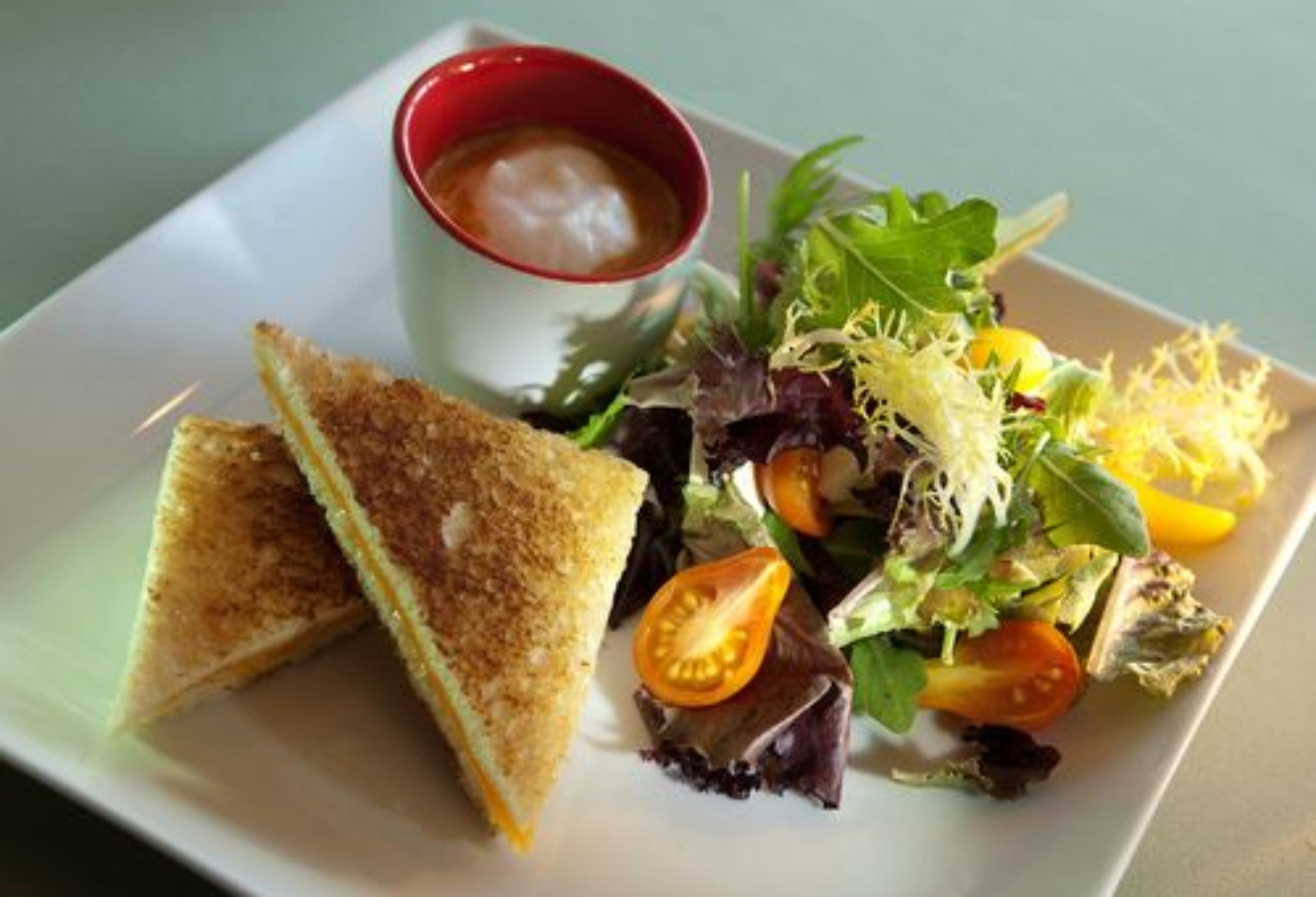 Un plato con un sándwich, una ensalada y una pequeña taza de salsa.