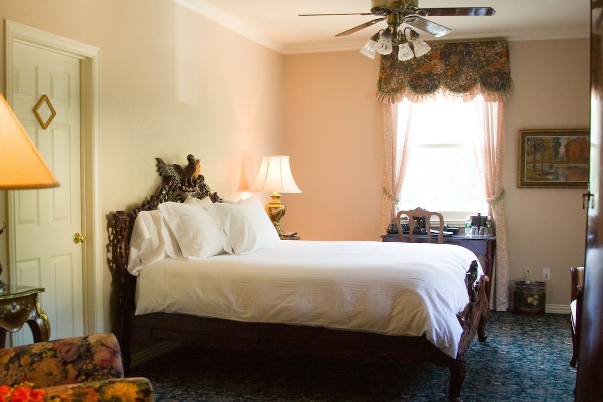 A bedroom with a bed, two bedside lamps, a chair, a desk, and a ceiling fan.