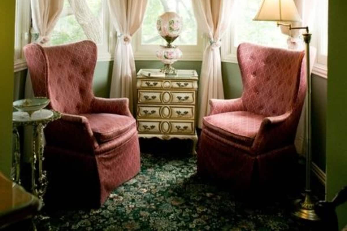 A room with two pink armchairs, a dresser with floral curtains, and a lamp.