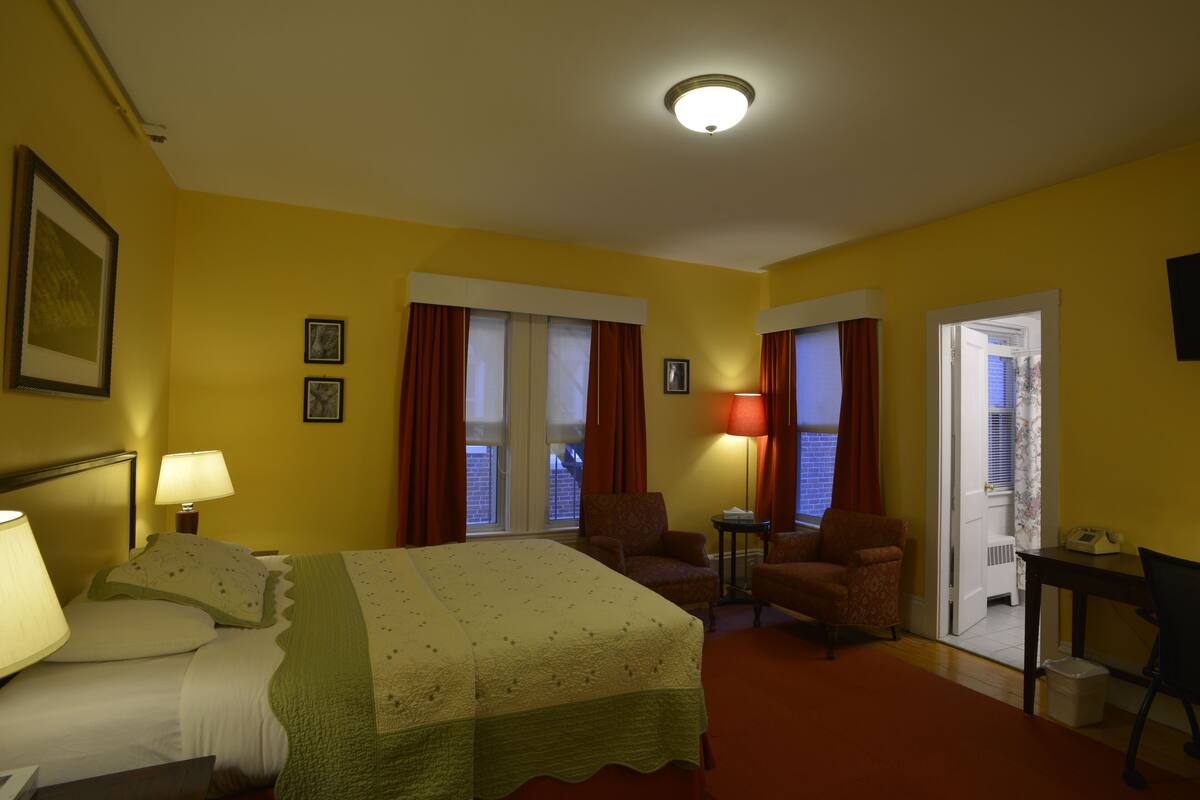 Habitación de hotel con cama, dos sillones, un escritorio y una puerta que da a un balcón.