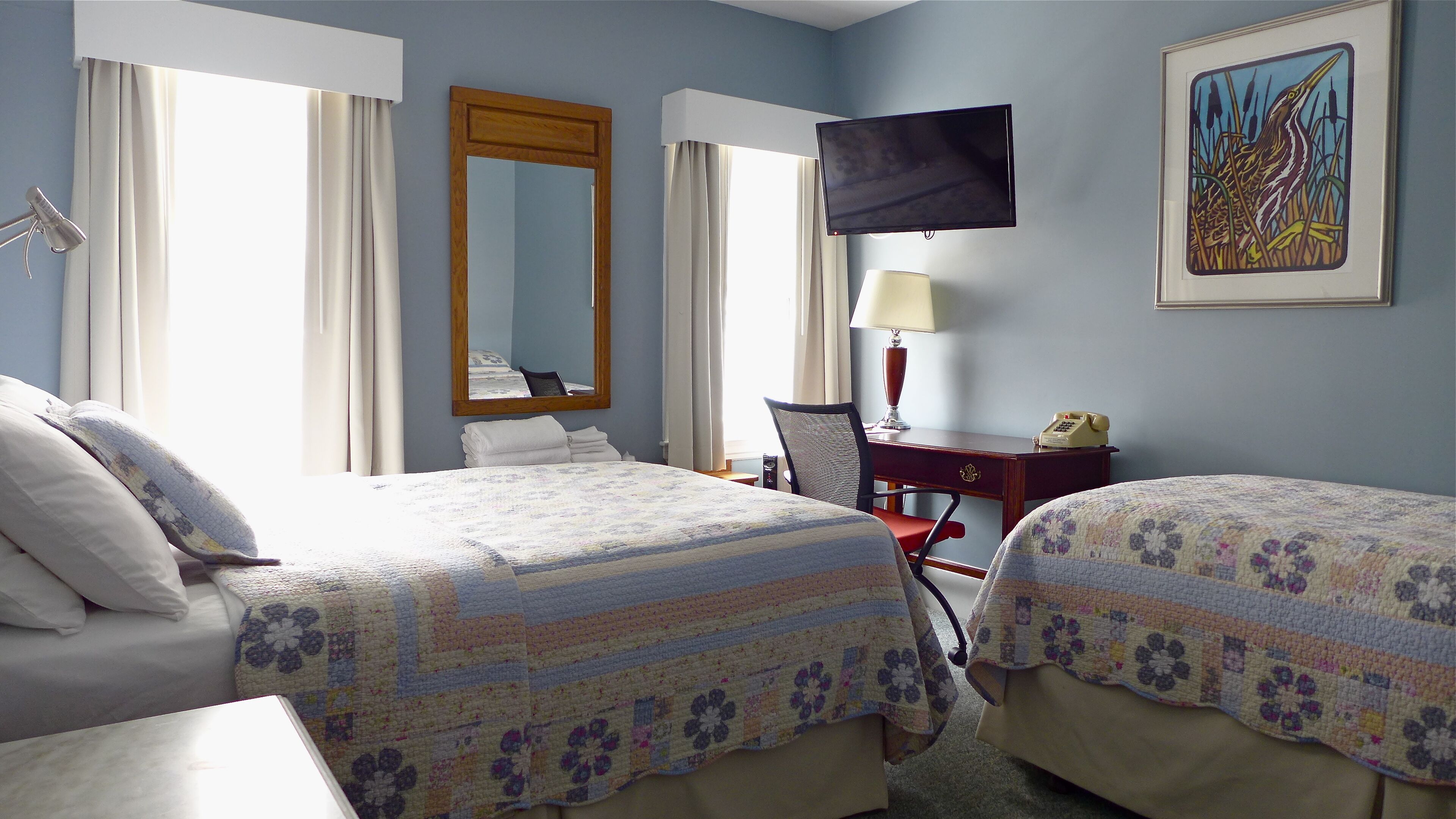 A hotel room with two beds, a desk, a chair, a TV, and a painting on the wall.